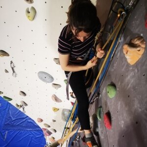 Un enfant s'entraînant sur un mur de bloc intérieur avec des prises colorées, en portant un t-shirt rayé et un pantalon foncé. Un tapis de chute bleu est visible en dessous.